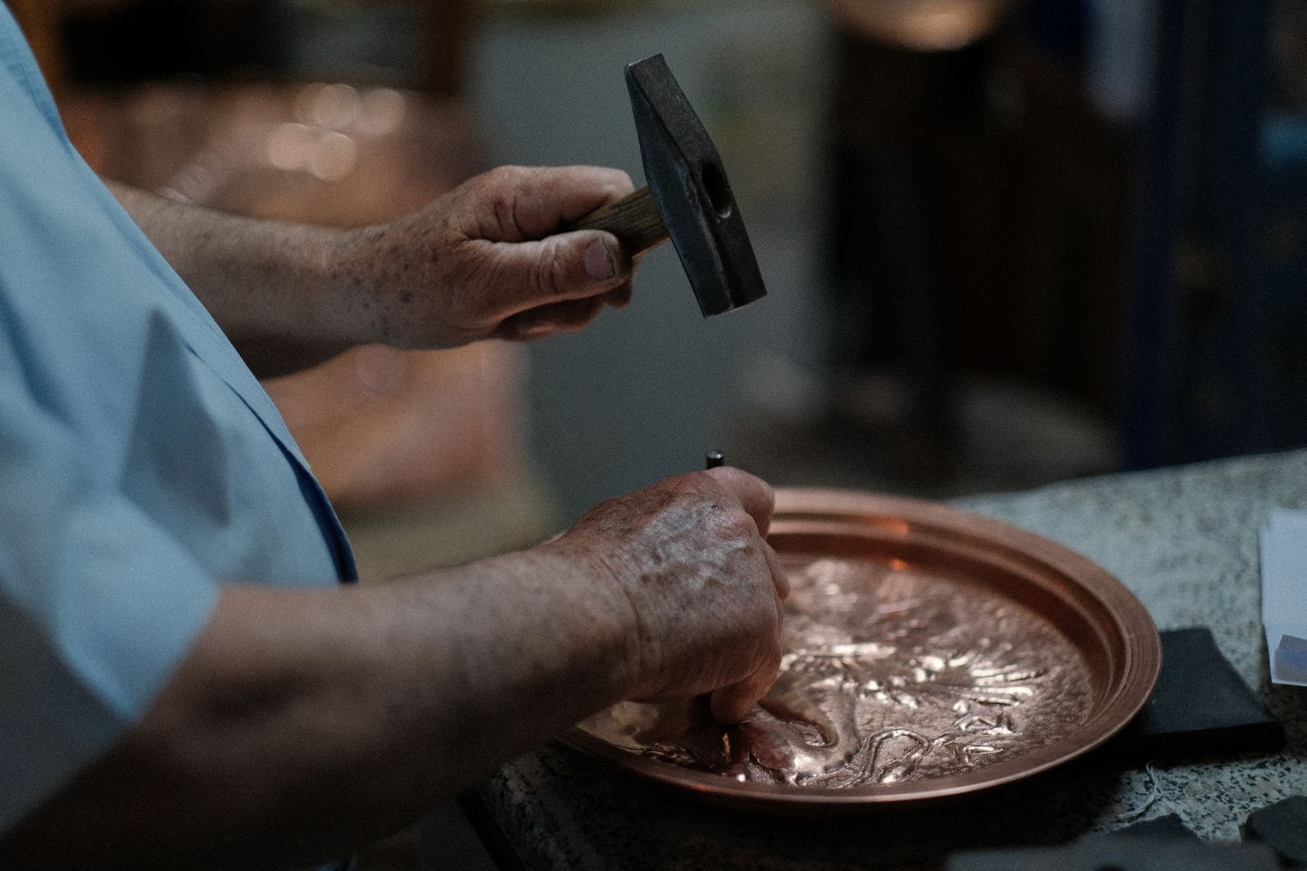 Close-up of skilled craftsman hand-hammering designs into a copper plate, showcasing traditional craftsmanship
