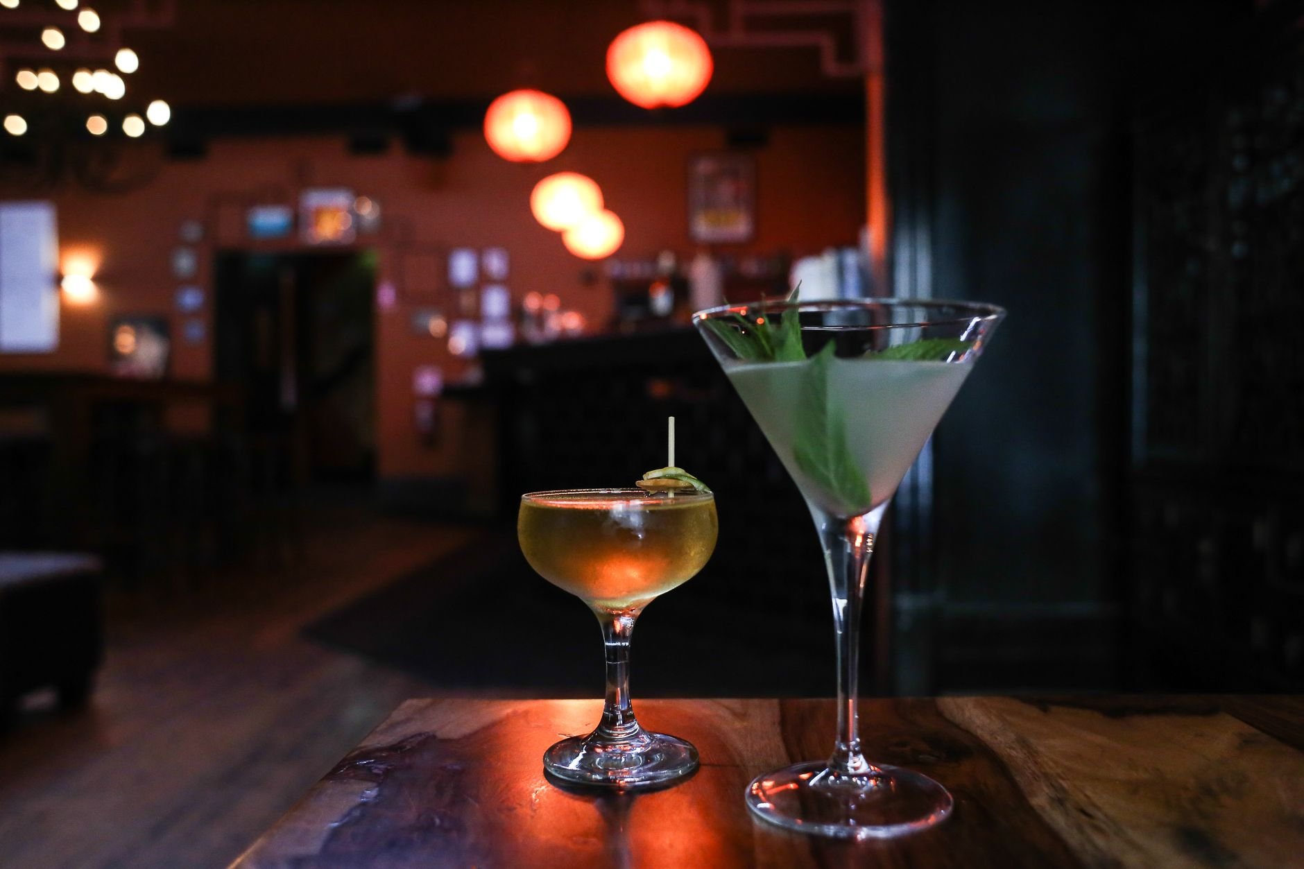 Two refreshing cocktails on a wooden table in a dimly lit bar with a warm ambiance